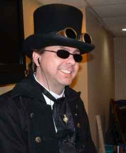 Author Mike Stewart in a top hat and goggles smiling as he runs a session of the Victorious RPG